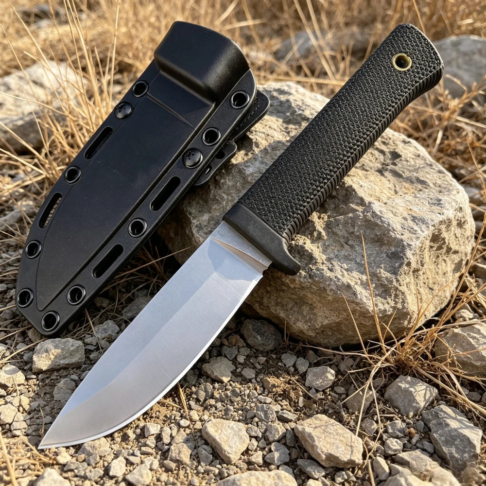 A black full-length stainless steel fixed blade outdoor knife resting on a rock amidst dry, sparse vegetation.
