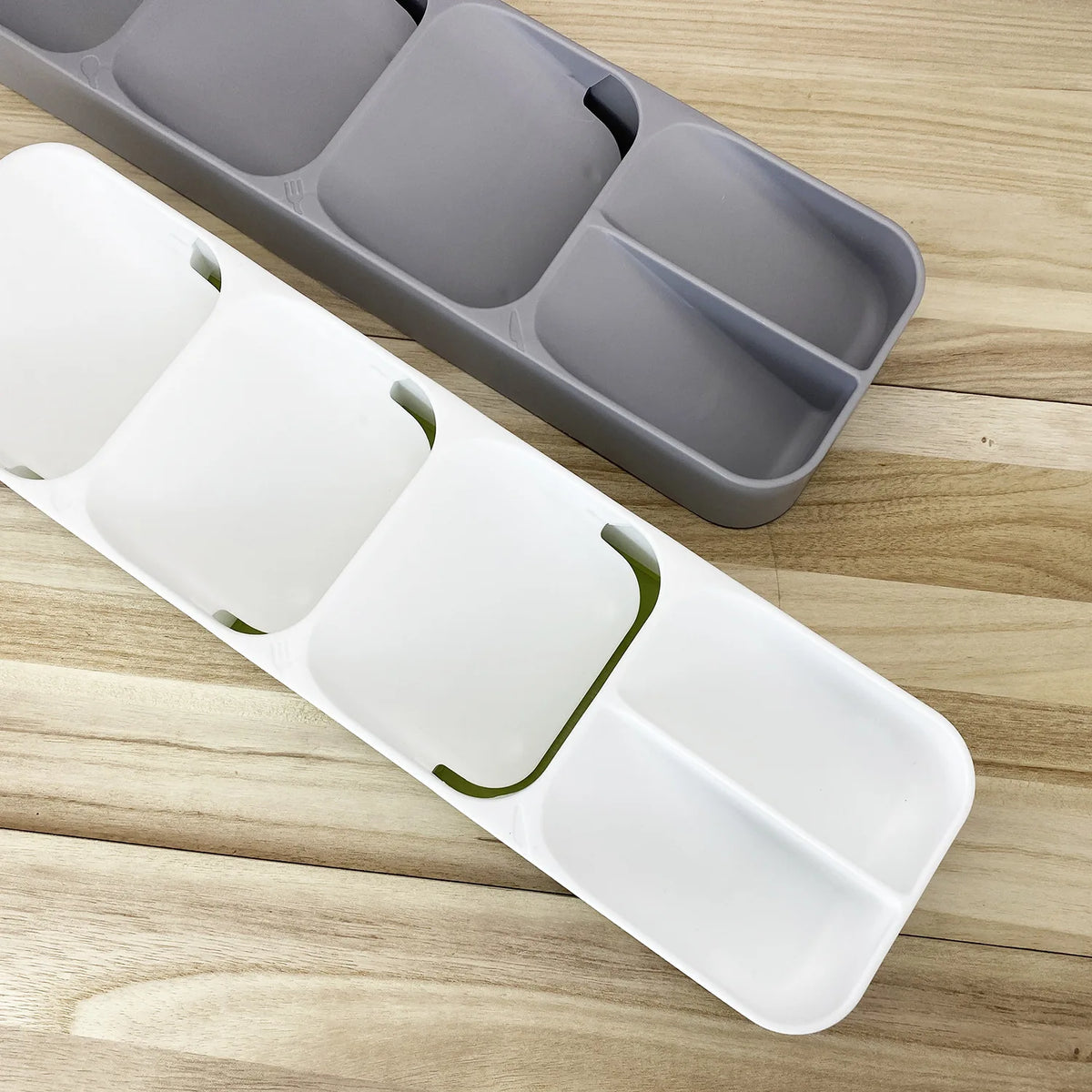 Un organizador de cubiertos compartimentado blanco y una bandeja gris sobre una superficie de madera.