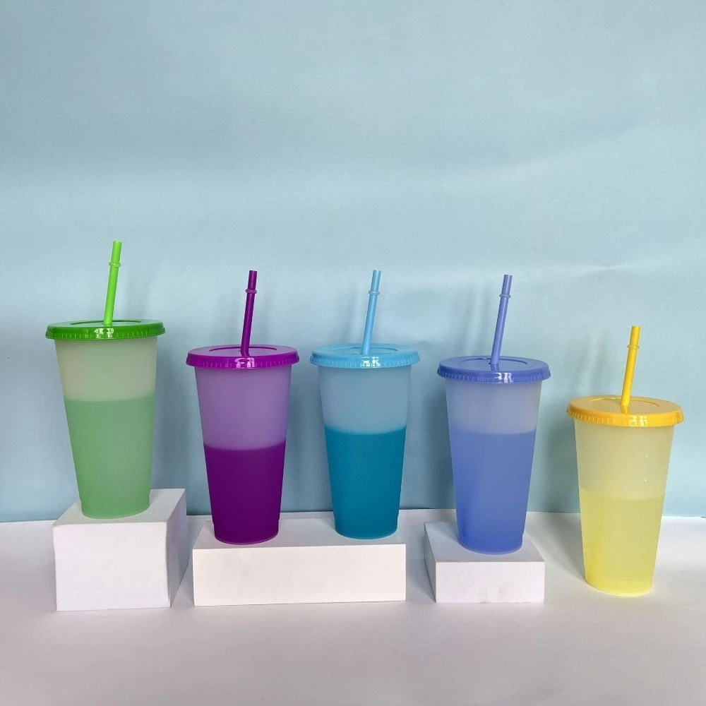 A set of ten colorful reusable tumblers in various shades of green, purple, blue, and yellow are displayed against a light bl