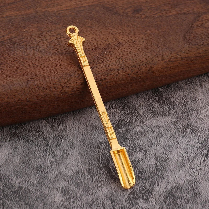 A gold-colored metal mini shovel spoon with a handle resting on a dark wooden surface.