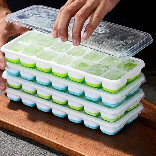 A hand is holding a stack of silicone ice cube molds with green and blue colored ice cubes on a wooden surface.
