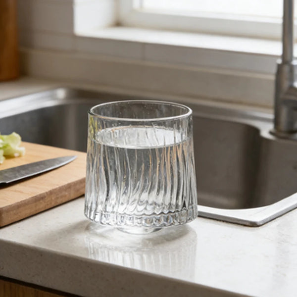 Ein klares Glas Wasser steht auf einer Küchenzeile neben einer Edelstahlspüle.