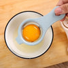 A hand is holding a light blue egg separator tool, which is positioned over a bowl containing a raw egg.