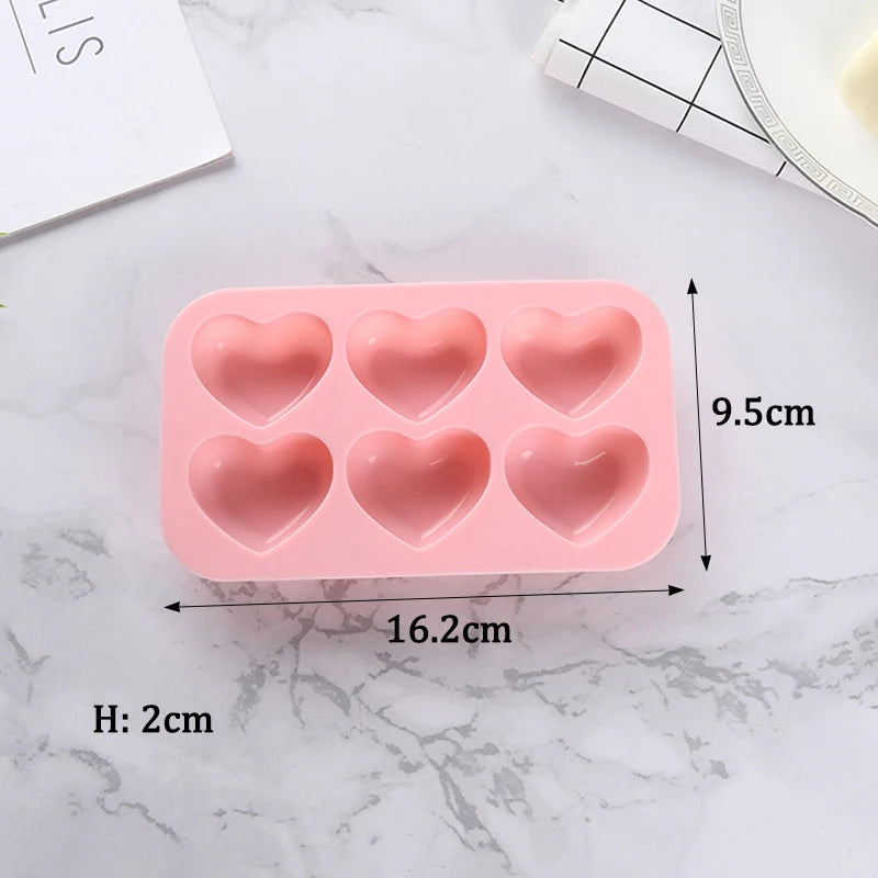A pink silicone heart shape baking mold with six cavities is shown on a white marble surface.