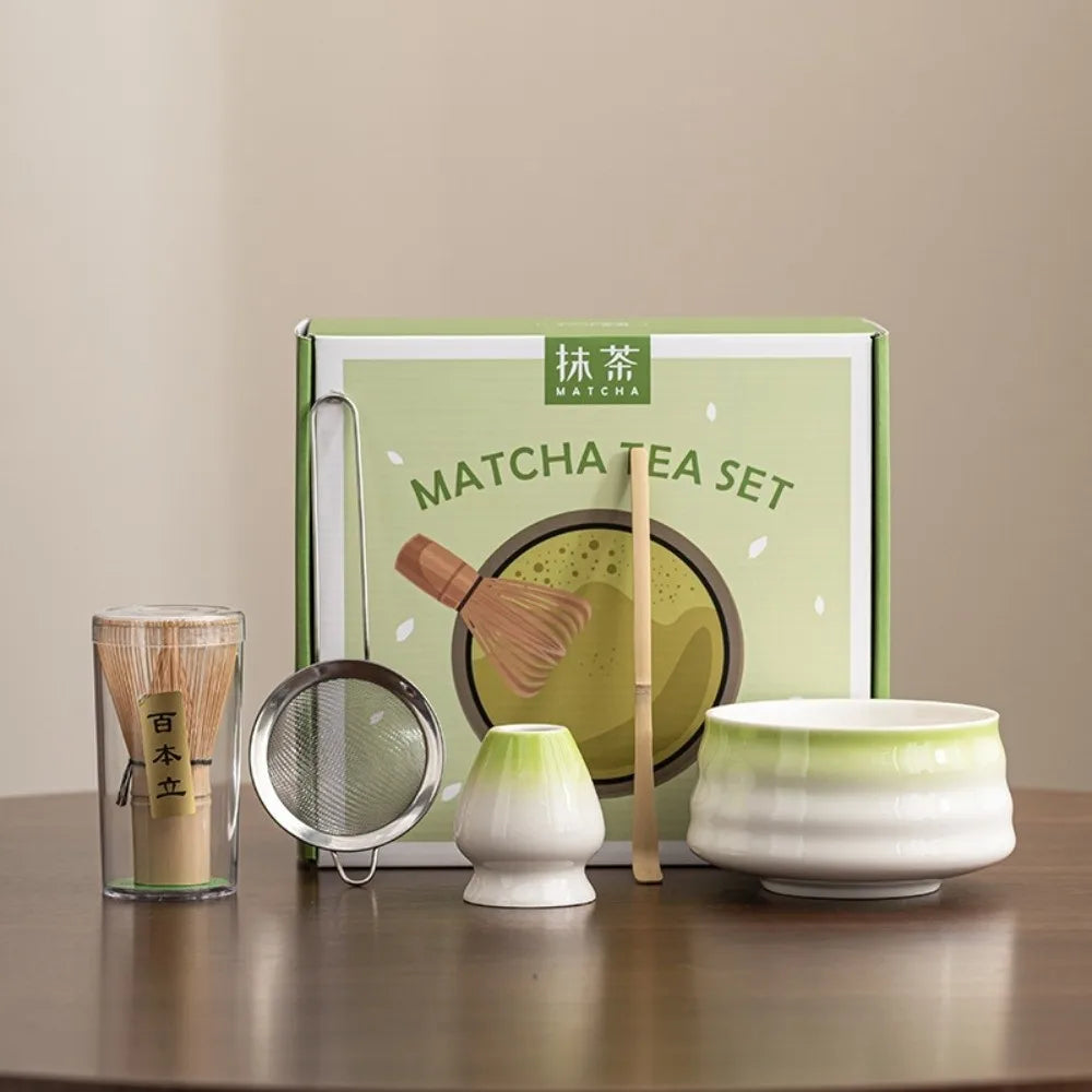 A green box containing a matcha tea set with a bamboo whisk, a tea bowl, and a bamboo scoop on a wooden surface.