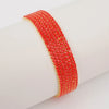 A red acrylic elastic bracelet with gold accents worn on a wrist.