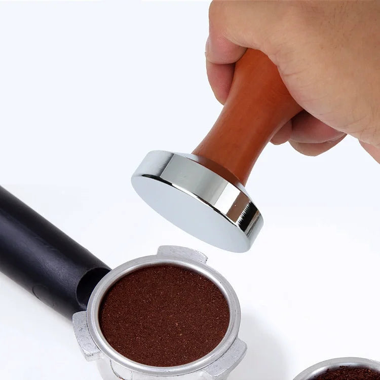 A hand is holding a precision espresso tamper set with a wood and stainless steel handle, showing the metal plunger and woode