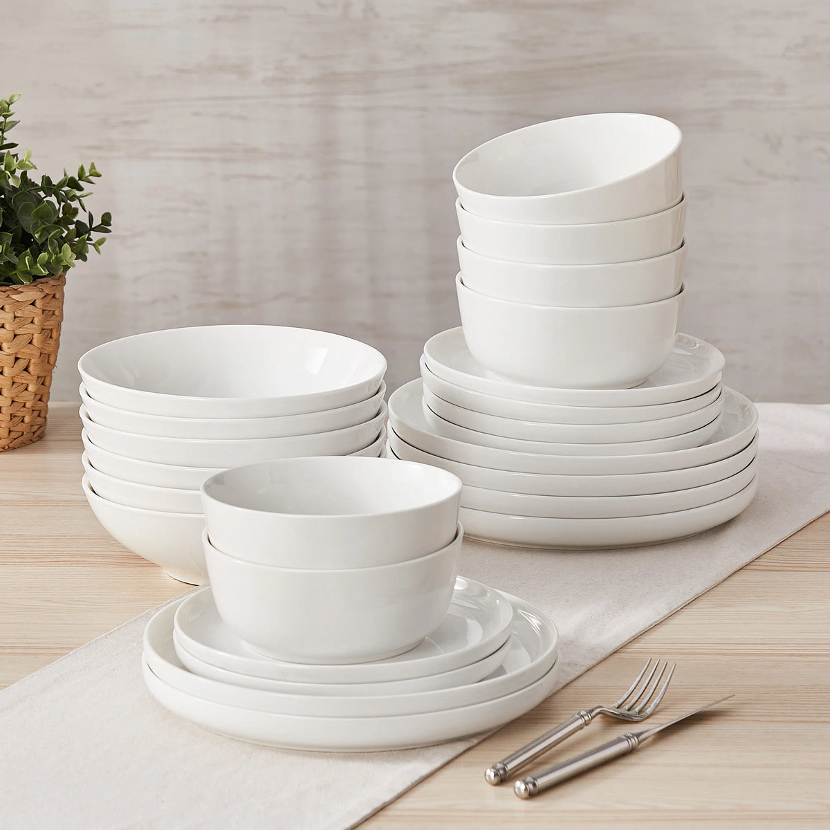 A stack of white porcelain dinnerware including plates and bowls on a wooden surface.