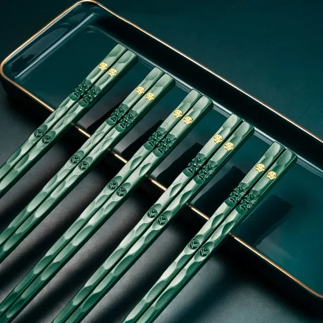 A set of reusable multi-color chopsticks with green and gold accents resting on a dark rectangular plate.