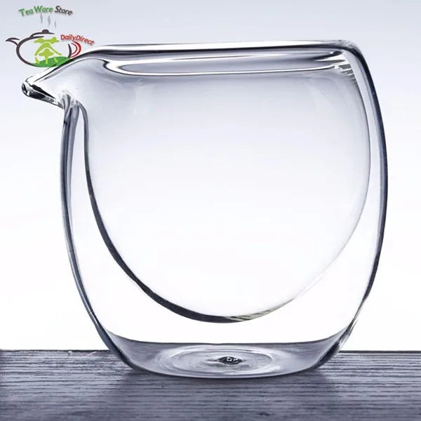 Clear double wall glass tea pitcher with a spout resting on a wooden surface.