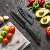 A black utility knife set with a blade and handle is displayed on a dark surface surrounded by fresh vegetables like tomatoes