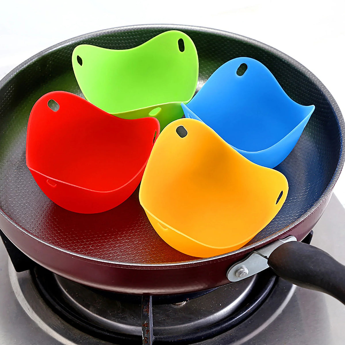 A silicone egg poacher set with three colored silicone molds resting on a dark cooking pan.