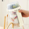 A hand holds a clear reusable container filled with overnight oats and snacks, displayed on a wooden rack.
