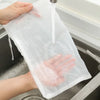 A hand is pouring liquid into a clear reusable mesh filter bag over a sink.