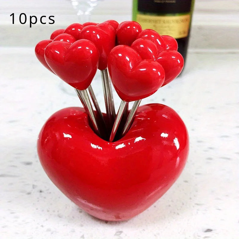 A set of ten red heart-shaped stainless steel fruit forks displayed on a white surface.