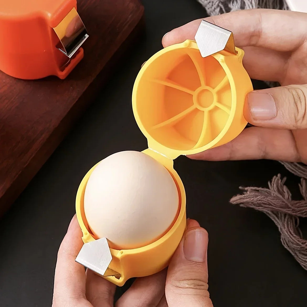 A hand holds an orange portable egg shell opener tool, separating a white egg.