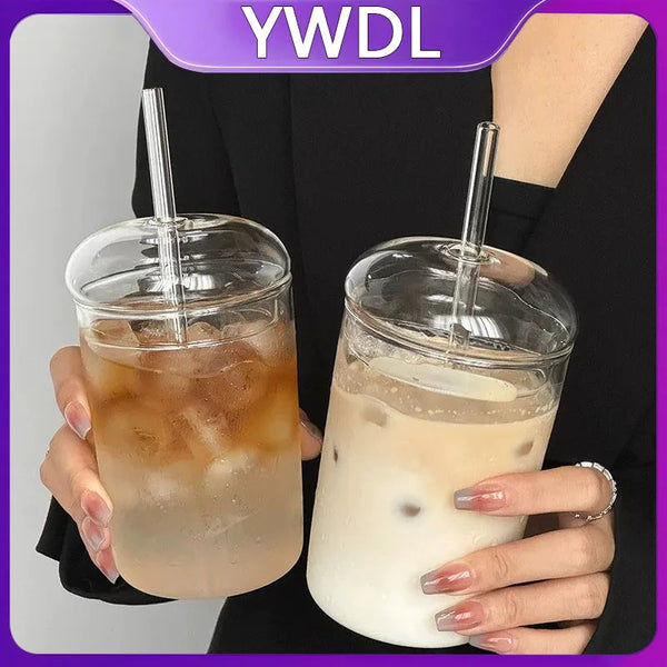 Eine Hand hält ein Glas Eistee in einem klaren Becher mit Strohhalm vor einem dunklen Hintergrund.