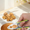 A hand holds a stainless steel nut cracker, demonstrating its use for cracking walnuts, pecans, and hazelnuts on a wooden sur