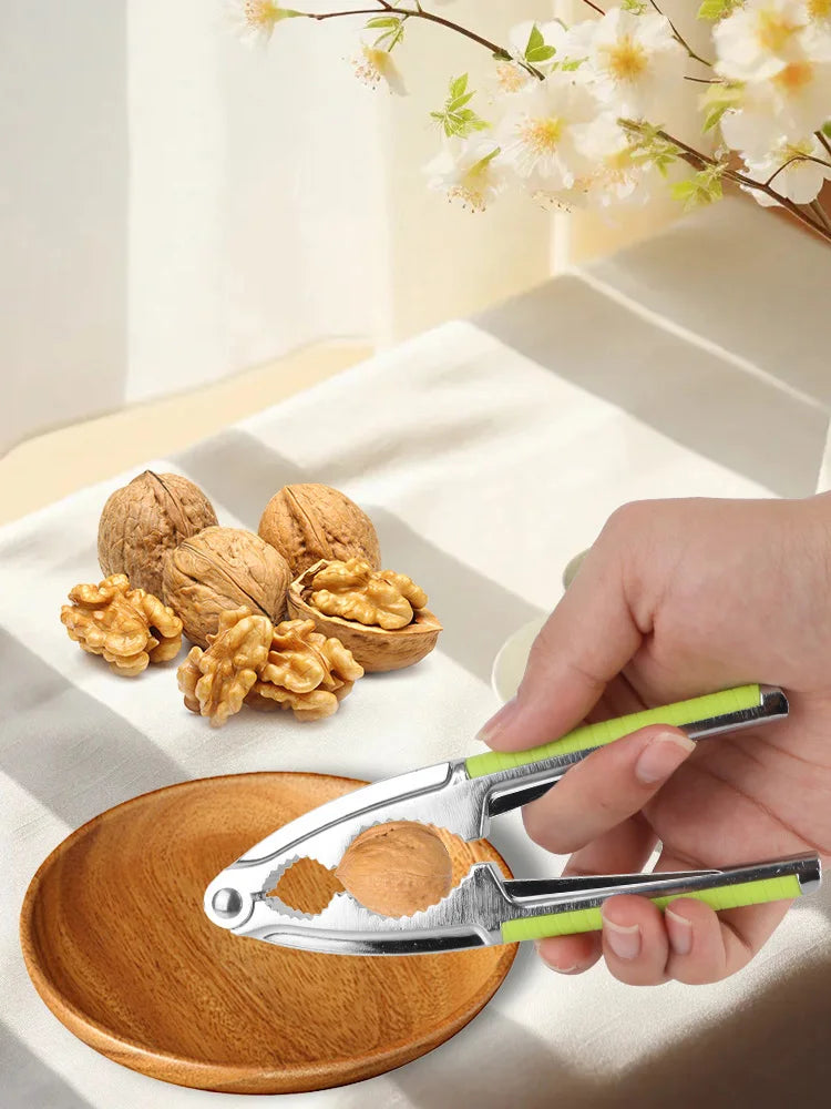 A hand holds a stainless steel nut cracker, demonstrating its use for cracking walnuts, pecans, and hazelnuts on a wooden sur