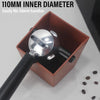 A silver espresso knock box with a black handle is shown inside a brown container.