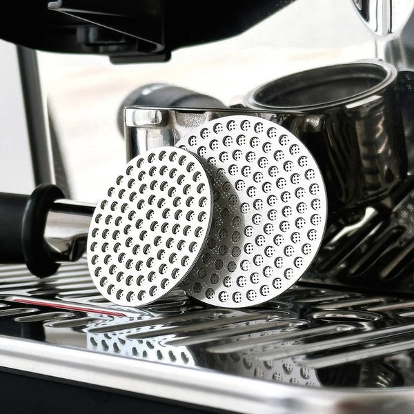 Two circular stainless steel reusable espresso filters resting on a metal drip tray.