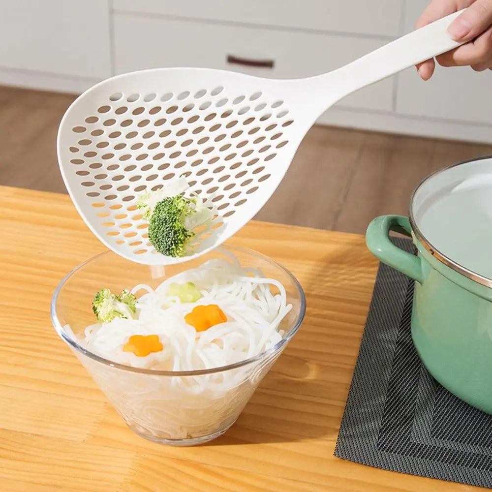 A white kitchen strainer and skimmer set is shown with shredded vegetables in a glass bowl on a wooden table.