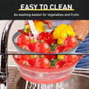 A hand is placing fresh tomatoes and fruits into a red silicone basket for washing.