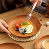 A wooden serving tray set features a plate with fresh fruit and a fork, resting on a woven mat.