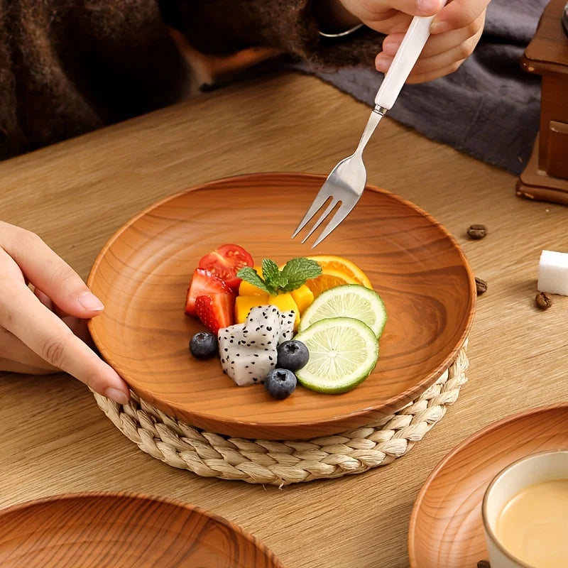 A wooden serving tray set features a plate with fresh fruit and a fork, resting on a woven mat.