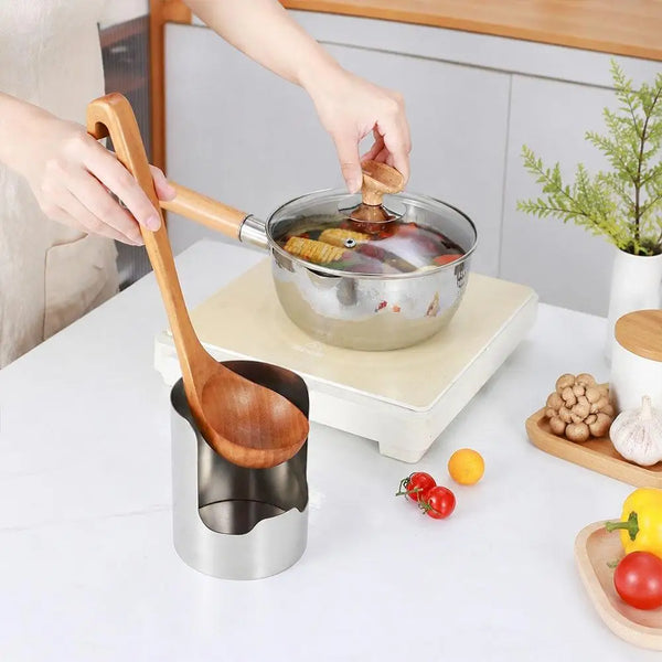 A hand is lifting a wooden spoon from a stainless steel pot, demonstrating a kitchen counter organizer for lids and utensils.