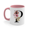 A pink ceramic coffee mug with a white background featuring a large black letter P decorated with floral elements.
