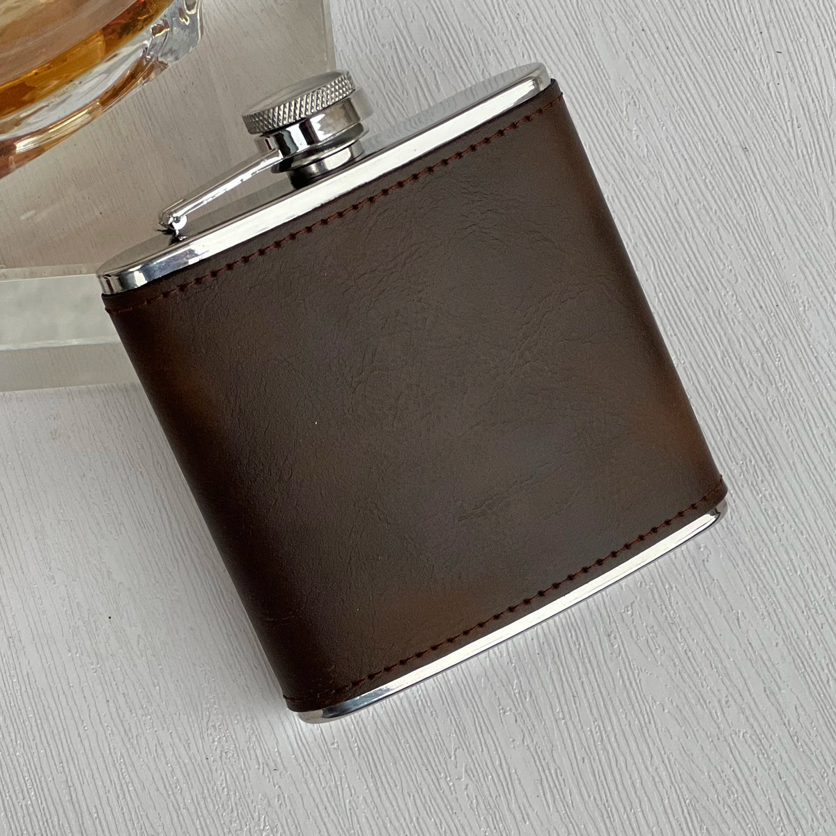 A stainless steel hip flask with a dark brown faux leather cover and silver accents.