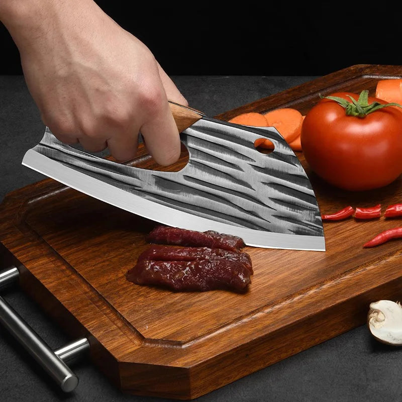 A hand is using a professional forged stainless steel chef knife to slice meat on a wooden cutting board.