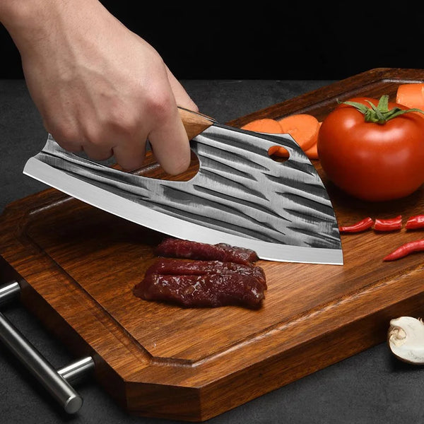 Eine Hand benutzt ein professionelles geschmiedetes Edelstahlkochmesser, um Fleisch auf einem Holzbrett zu schneiden.