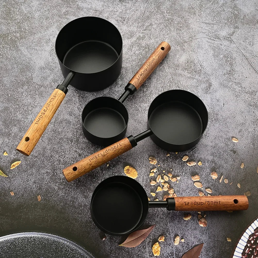 A set of black stainless steel measuring spoons with wooden handles scattered on a gray surface.