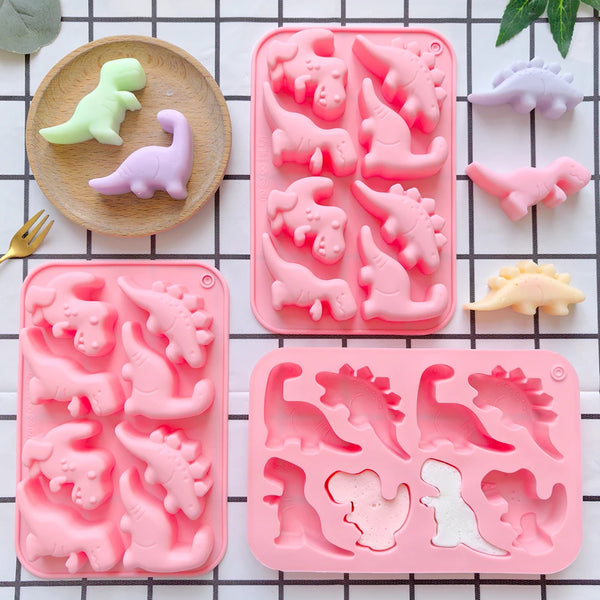 A pink silicone mold with eight cavities shaped like dinosaurs, including a green and purple dinosaur in the background.