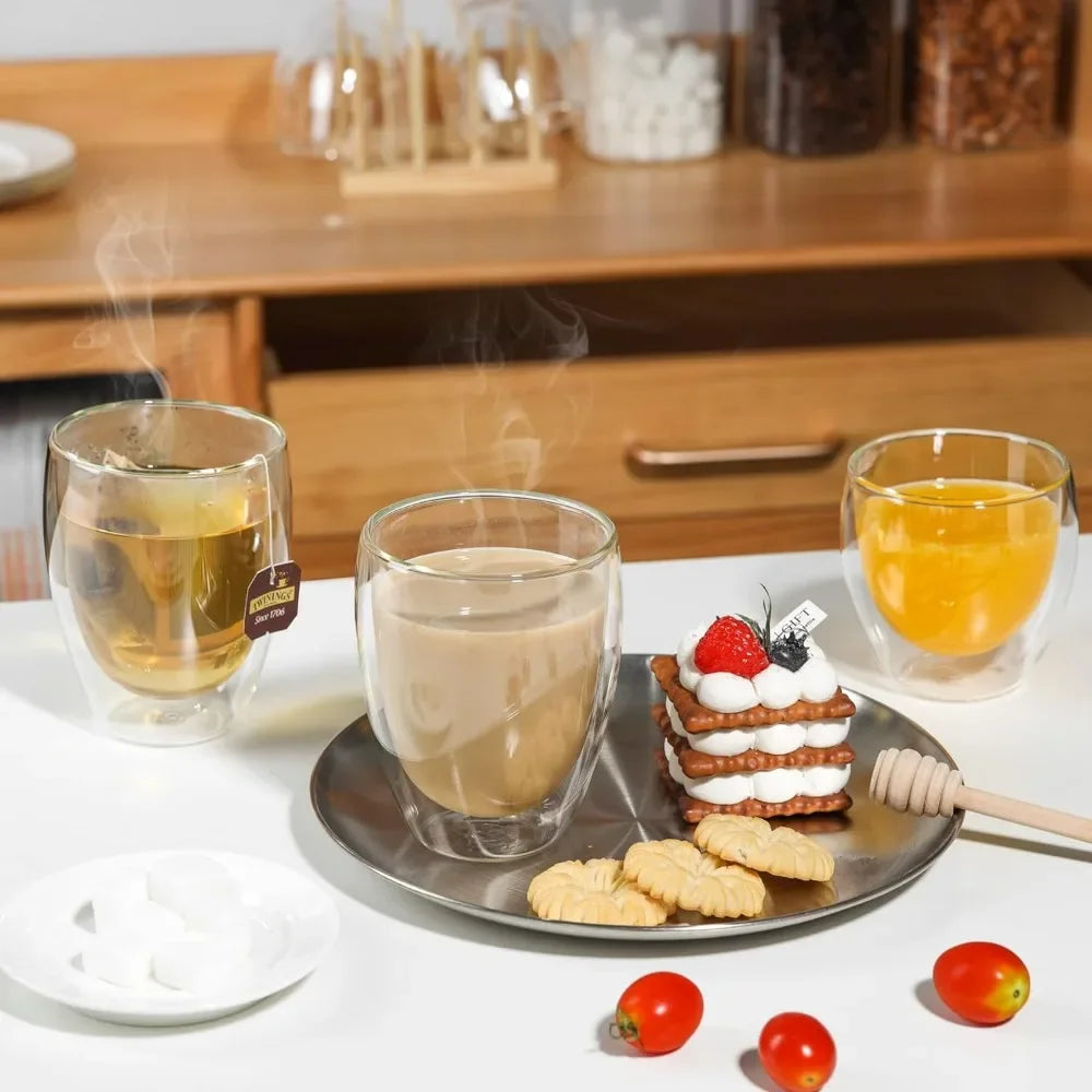 A set of insulated double-wall glass coffee mugs with brewed tea and fresh fruit on a white table.