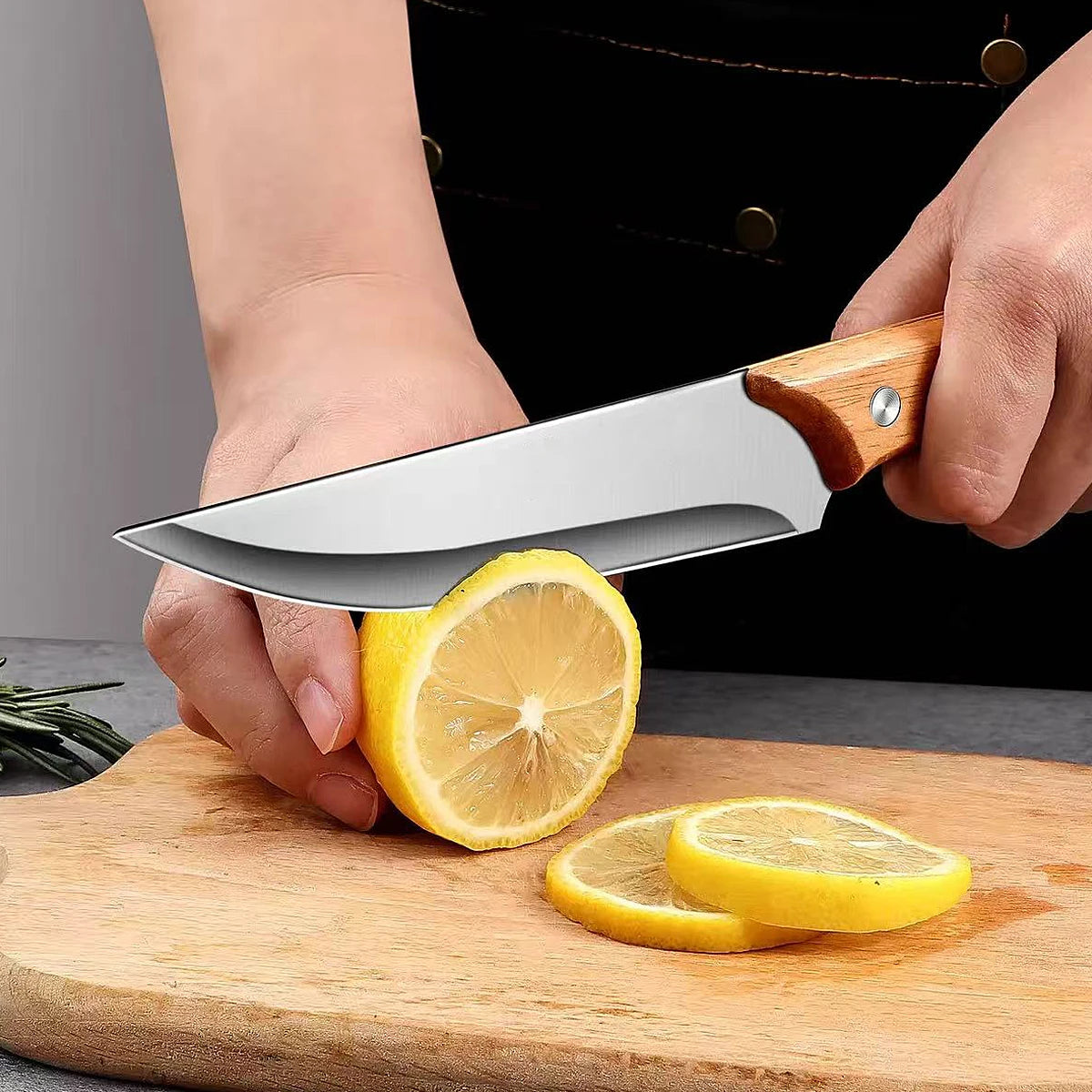 A hand holds a stainless steel fillet boning knife slicing through a lemon on a wooden cutting board.