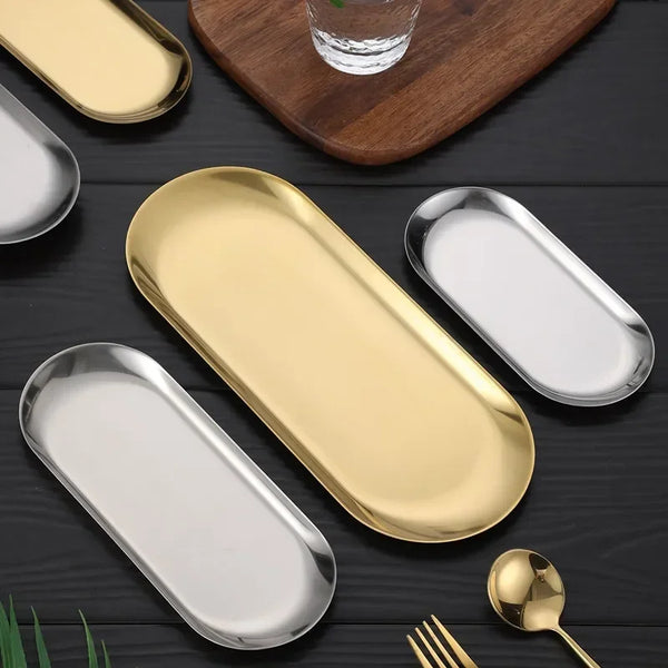 Ein Set eleganter Edelstahl-Dessertplatten in Gold- und Silbertönen auf dunkler Oberfläche.