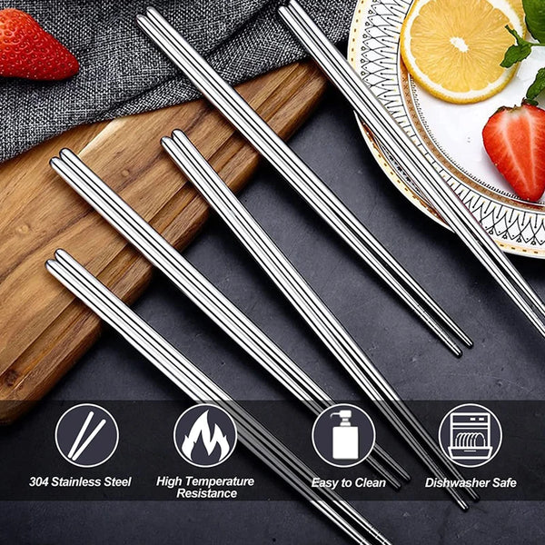 A set of stainless steel chopsticks resting on a wooden board with fresh strawberries and a slice of orange.