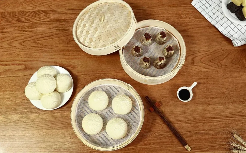A wooden table displays various food items, including steamed buns and small savory bites, arranged in bamboo steamers.