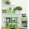A set of elegant green glass teacups and mugs displayed on a wooden counter with a coffee maker.