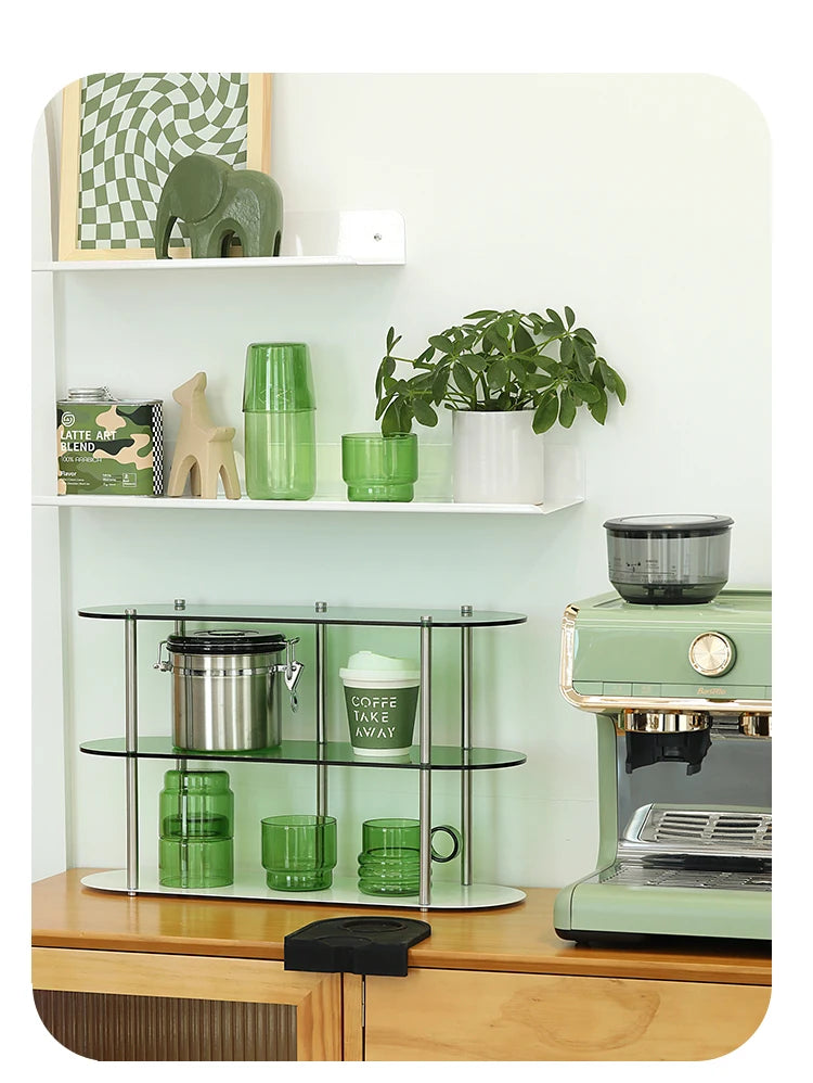 A set of elegant green glass teacups and mugs displayed on a wooden counter with a coffee maker.