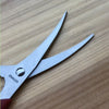 A pair of stainless steel seafood kitchen scissors lying on a wooden surface.