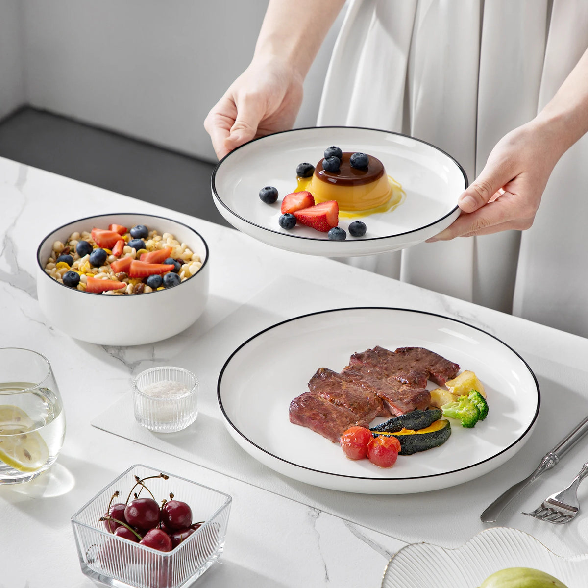 Hands are presenting a plate of grilled steak and vegetables on a white ceramic dinner plate.