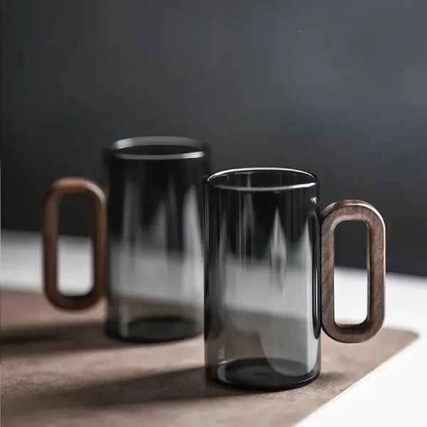Smoke gray glass drinking cup with a wooden handle resting on a light surface.