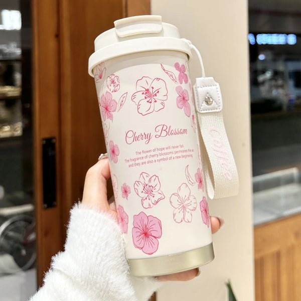 A hand holds a white insulated travel mug with pink cherry blossom floral design.