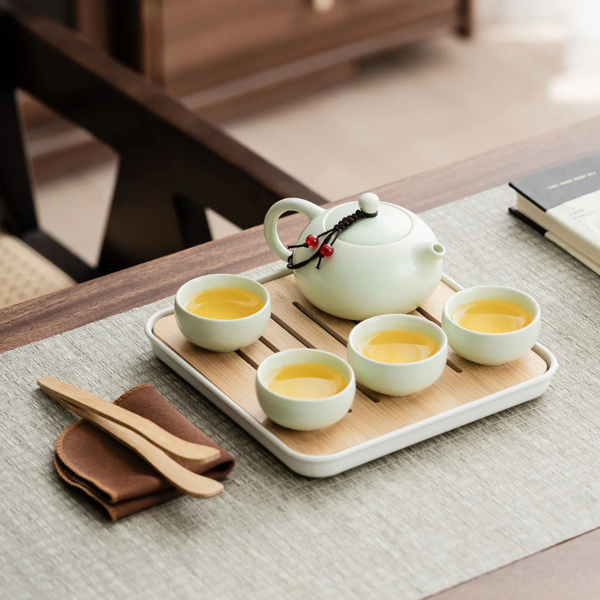 A white ceramic tea set with a teapot and four small cups is displayed on a wooden tray on a light gray table.