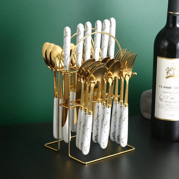 A gold-toned cutlery set with marbled white handles is displayed on a stand next to a bottle.