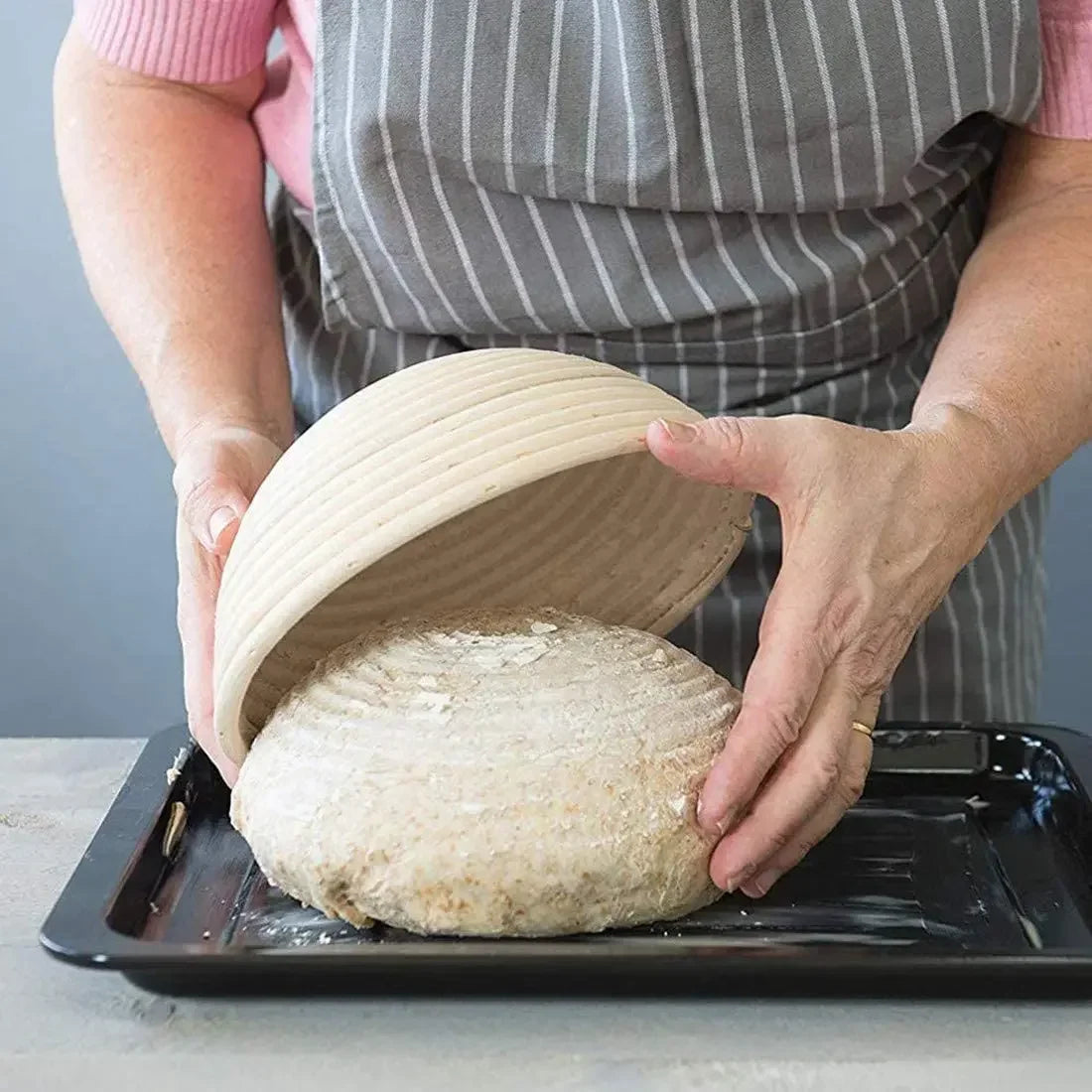Hands holding an open natural rattan bread proofing basket filled with light-colored bread.